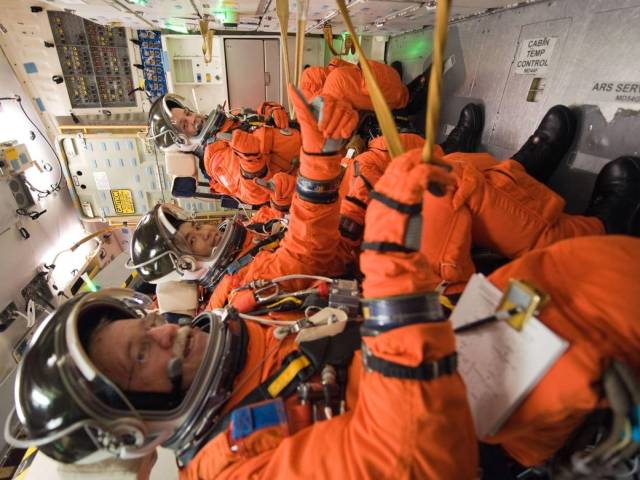 Four astronauts in orange spacesuits seated on their backs during training