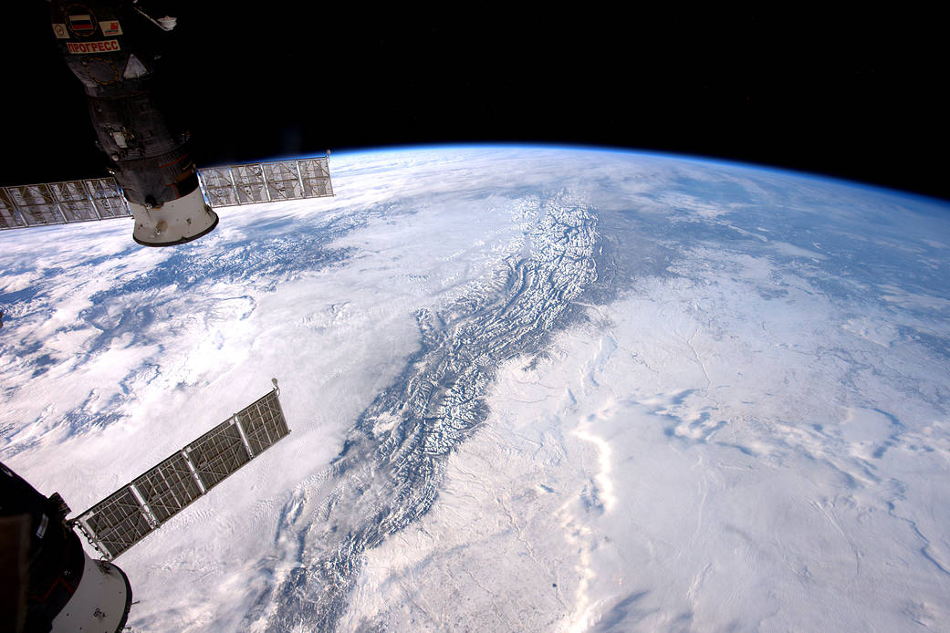 Rocky mountains visible through clouds from the International Space Station with Soyuz spacecraft visible at left of frame