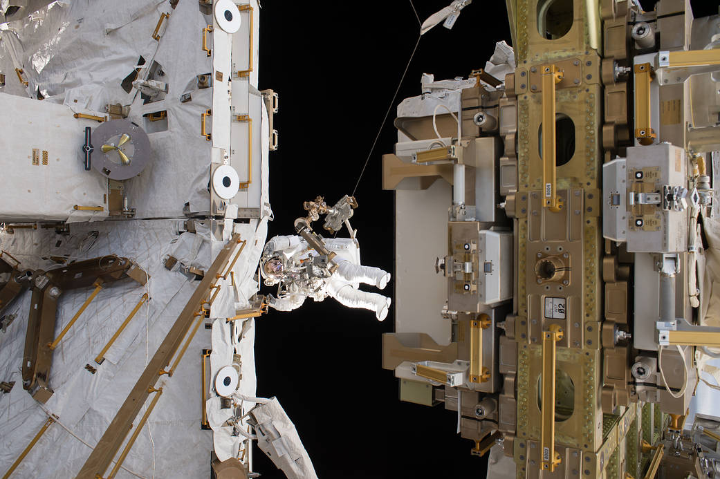 Astronaut in spacesuit at work outside space station with modules at either side of frame
