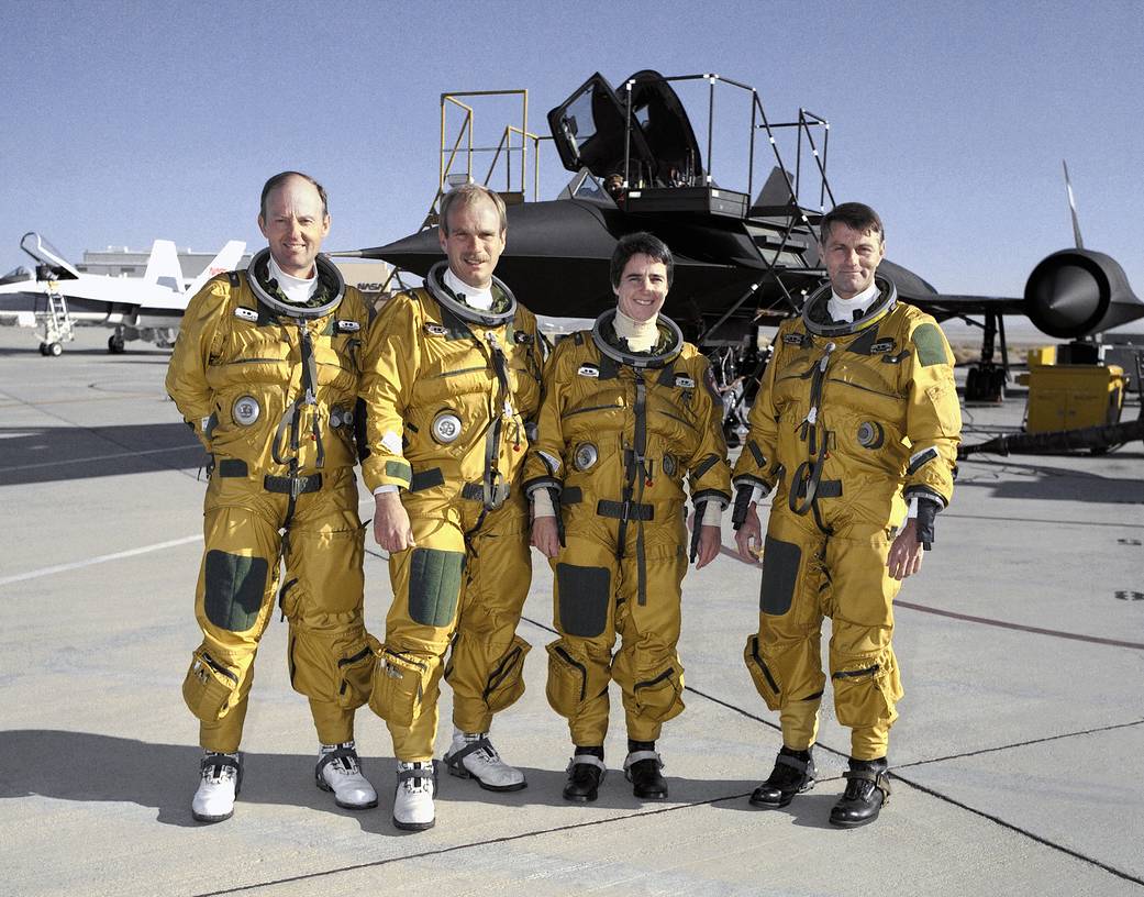 Pilots and crew wearing spacesuits stand in front of the SR-71 Blackbird aircraft.