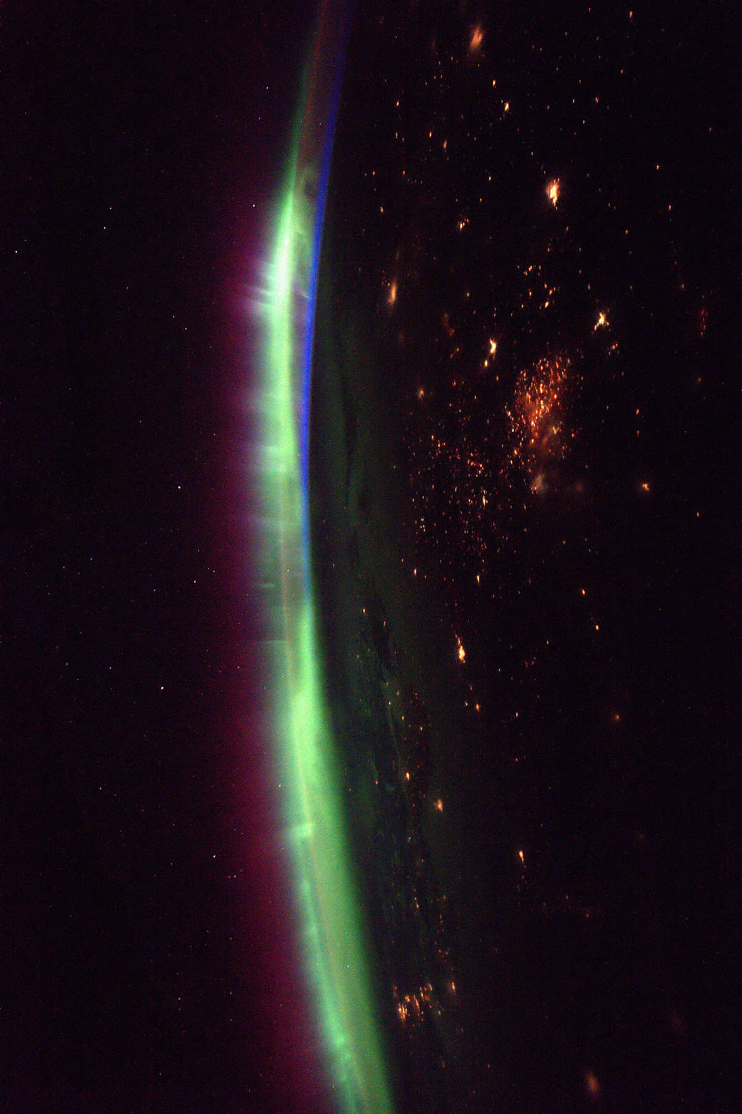 Aurora glowing on Earth's horizon with nighttime lights visible below