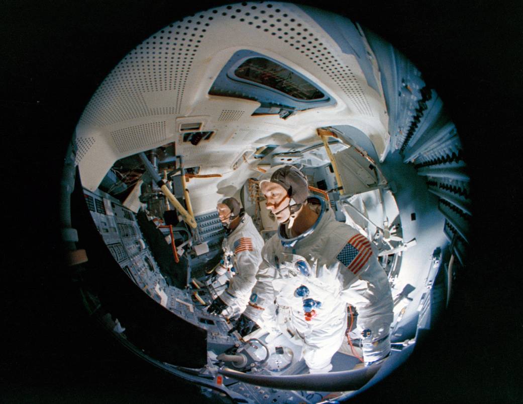This fish-eye camera lens view of the interior of the Apollo Lunar Module Mission Simulator at the Kennedy Space Center is one of several selected by the Apollo 9 crew to appear in "Apollo: Through the Eyes of Astronauts." In the foreground is mission commander James McDivitt; in background is Russell Schweickart, lunar module pilot.
