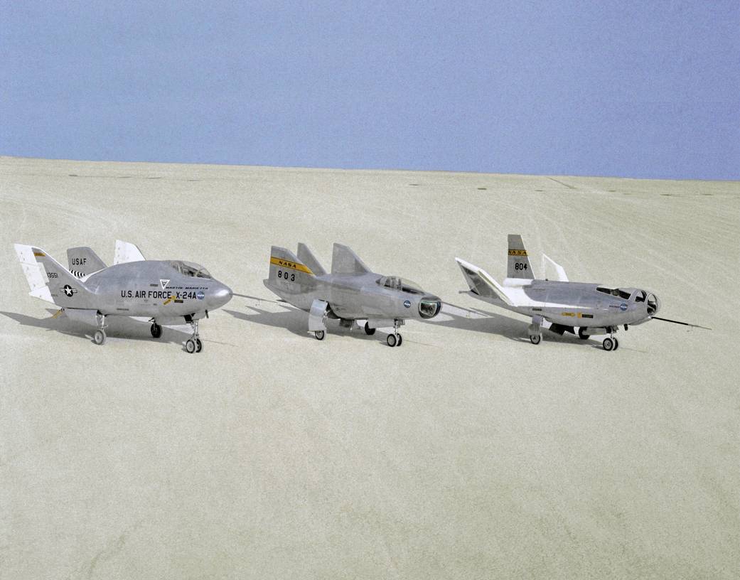 Three aircraft are in a row on a dry lakebed.