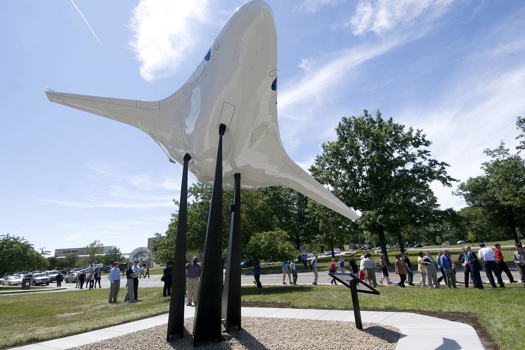 Model of aircraft with large cone shaped body and two small curved wings near back raised on stand outside