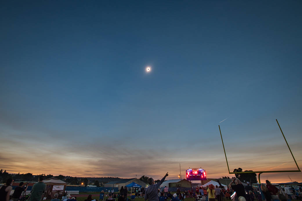 A total solar eclipse is seen Monday, August 21, 2017 in the sky with spectators below watching on football field