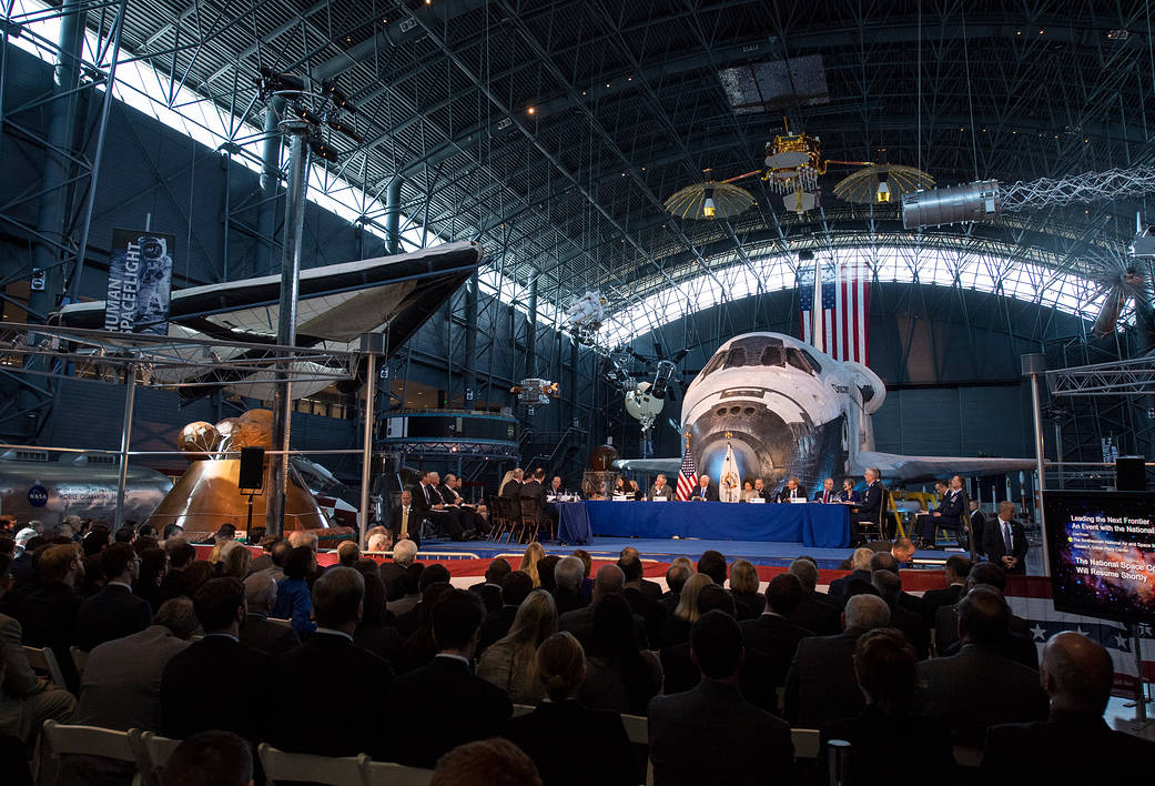Space Council members at tables in front of Shuttle Discovery inside museum