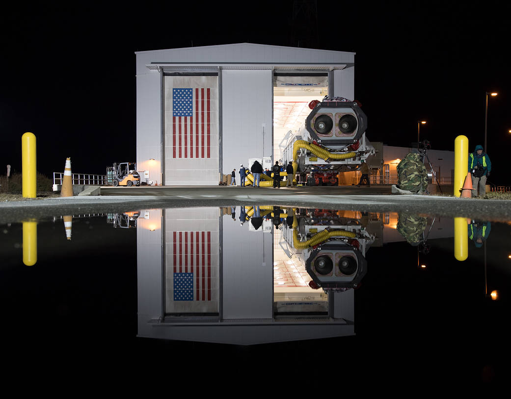 Antares rocket reflected in water as it rolls out to launch pad