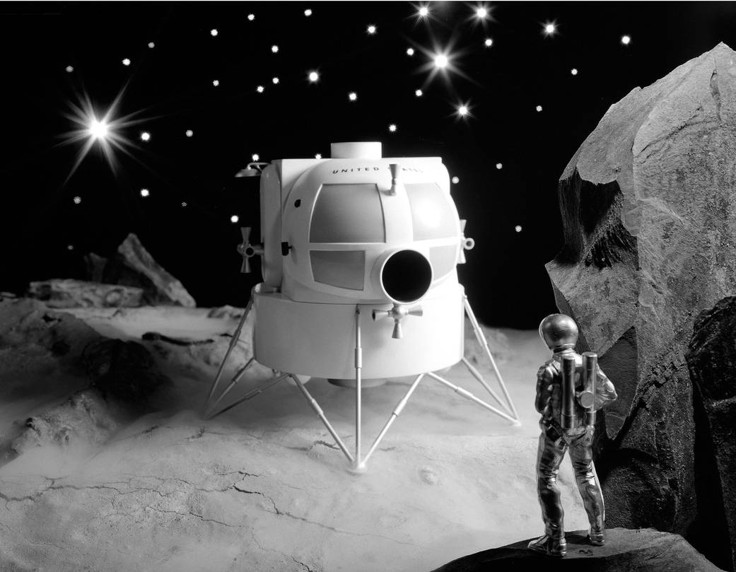 Model in white of lunar lander concept on surface with model astronaut at side and stars in background