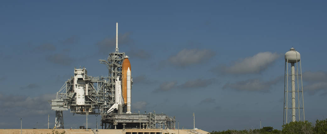 Wide shot in daytime of shuttle Discovery vertical on launch pad with tower