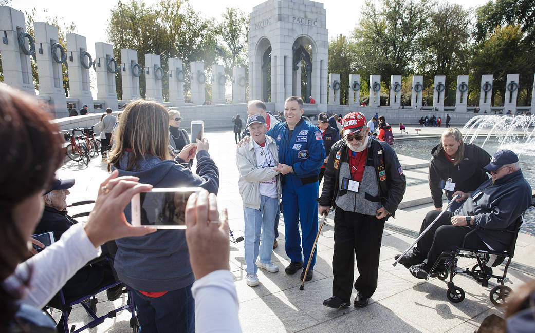 Astronaut Fischer in blue jumpsuit at World War II memorial poses for photo with veterans