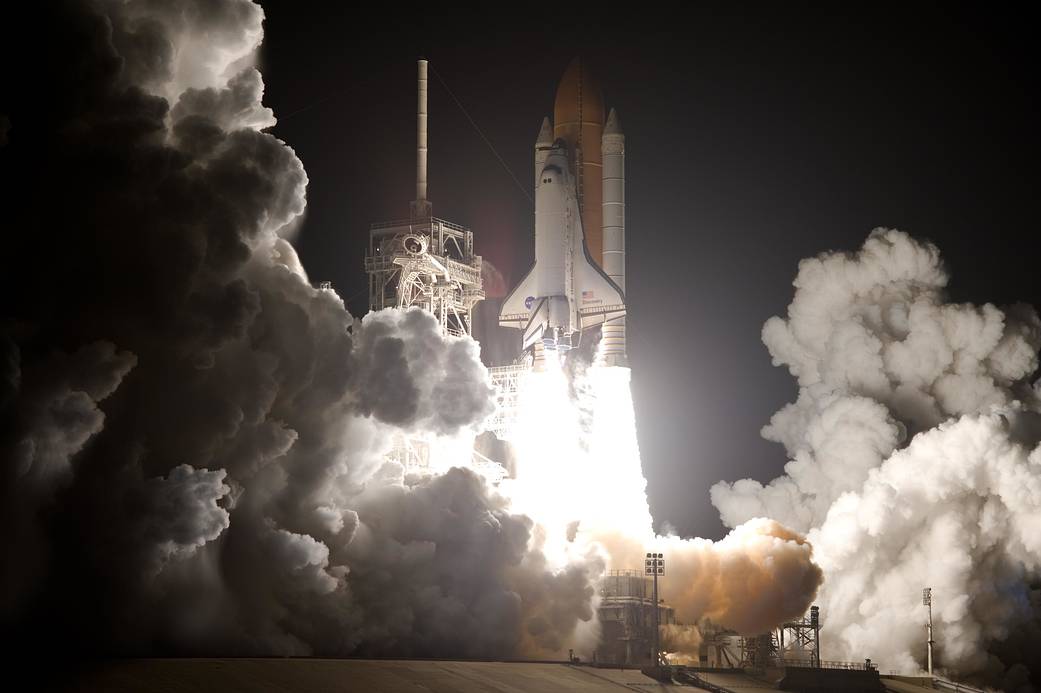 Close view of nighttime shuttle launch with clouds of smoke at bottom of image