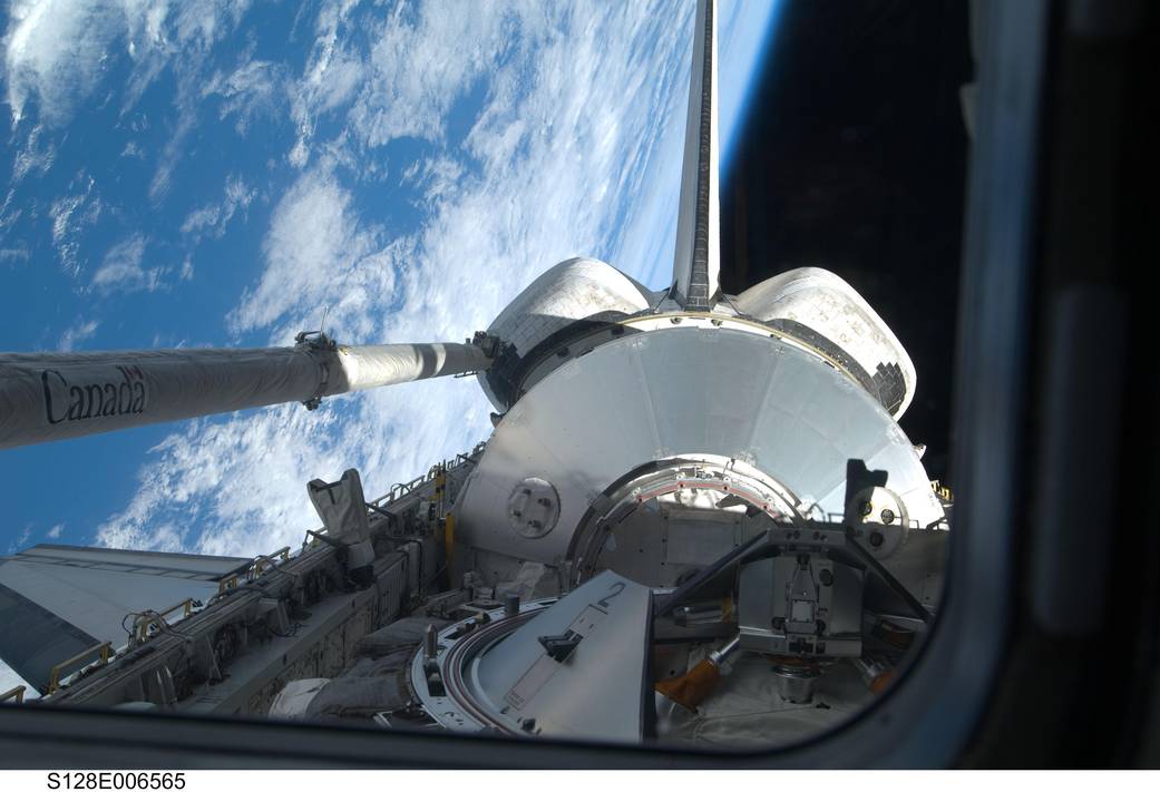 Tail end of shuttle Discovery with bay doors open and robotic arm at left, with Earth visible below