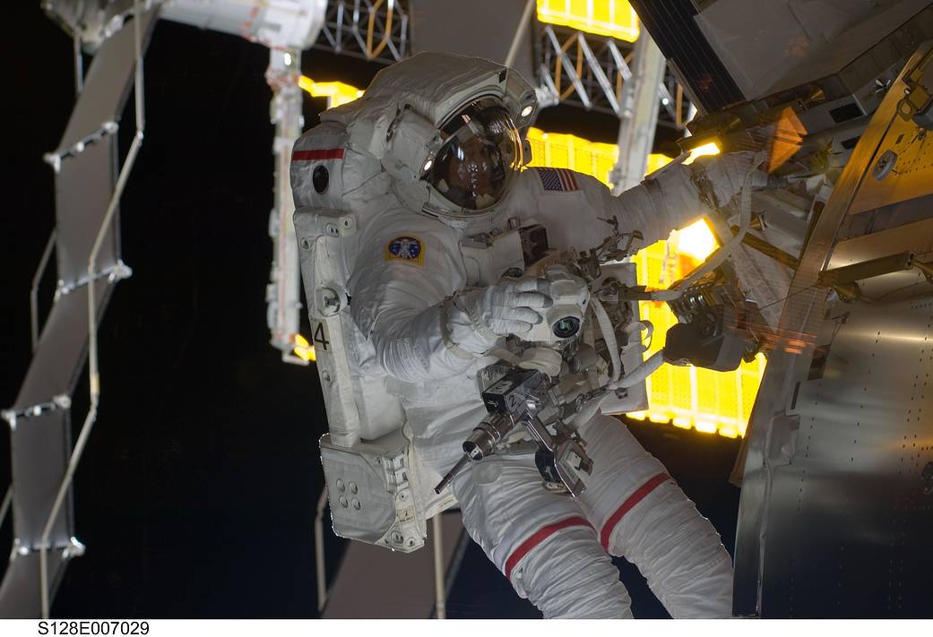 Spacewalking astronaut working outside space station with solar arrays visible in background