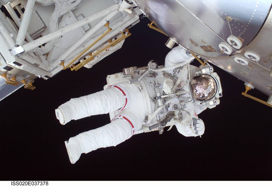 Spacewalking astronaut in spacesuit floating sideways outside space station module at top