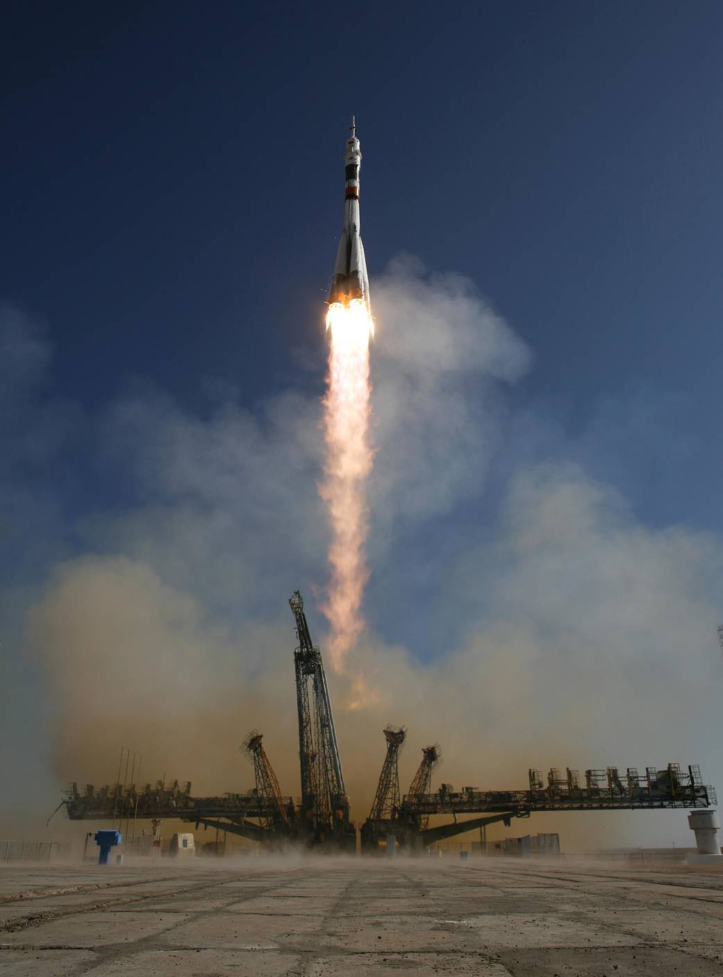 Launch of Soyuz rocket against dark blue sky with pulled back launch tower surrounding
