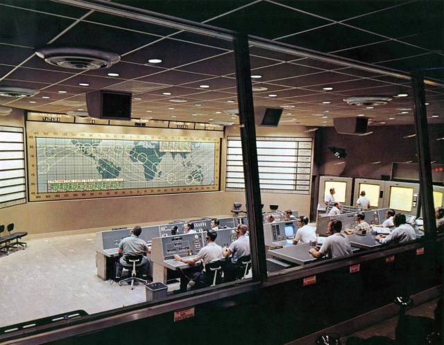 Behind the Flight Control area in Mercury Mission Control was a glass-enclosed viewing section that consisted of two levels, with rows of chairs and standing room at the back.