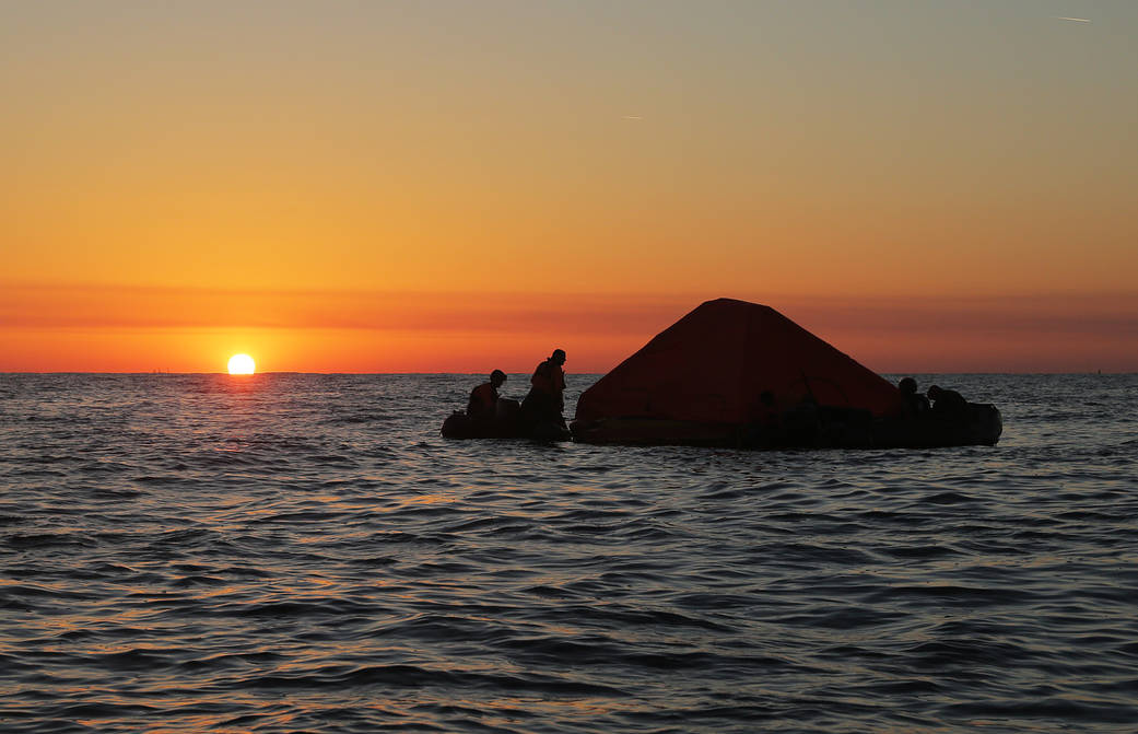 Pararescue specialists secure a covered life raft as the sun sets during an astronaut rescue training exercise