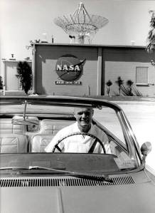 Astronaut John H. Glenn sits in a car in front of the east side of the Mercury Mission Control building.