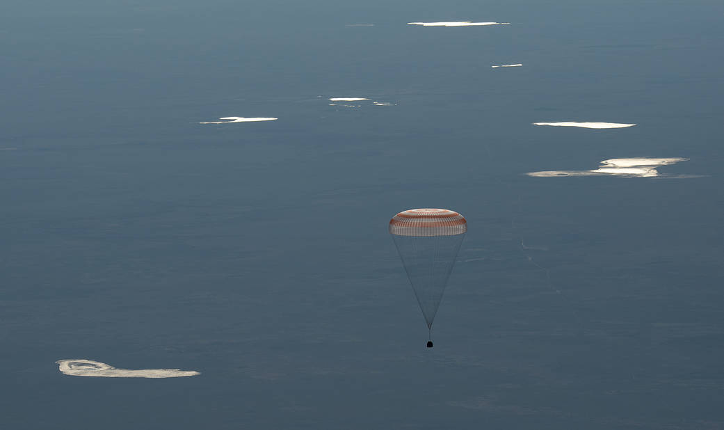 Soyuz capsule descends toward Earth with parachute deployed
