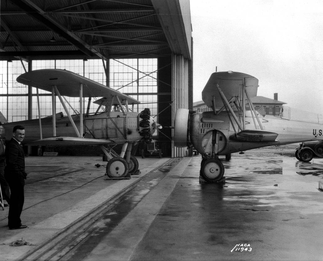 This image shows NACA chief test pilot Melvin Cough outside a hangar at the Langley Memorial Aeronautical Laboratory. The test vehicle on the right is a Curtiss BF2C-1 Goshawk.