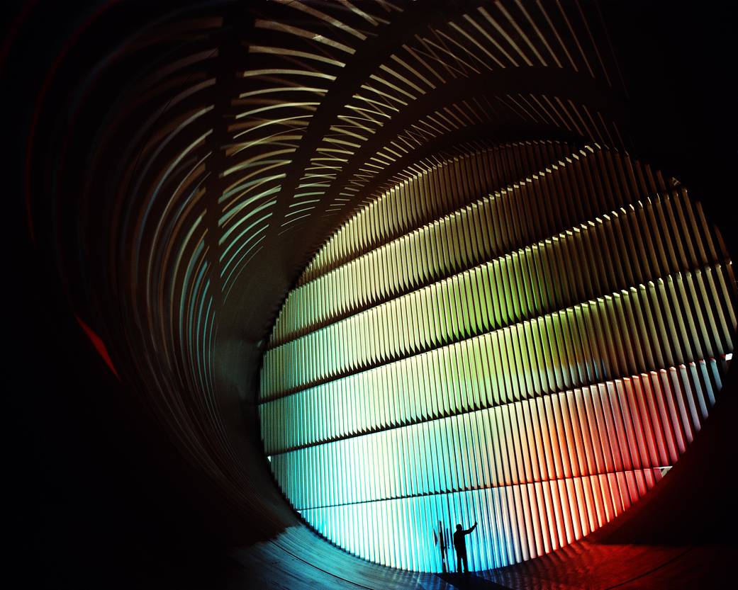 Inside the 16-foot transonic wind tunnel with colorful lights from blue, orange, red and green. At the bottom of the image is a technician unlatching the door.
