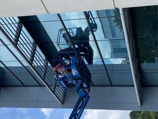 Two people up on a lift outside a building near the windows.