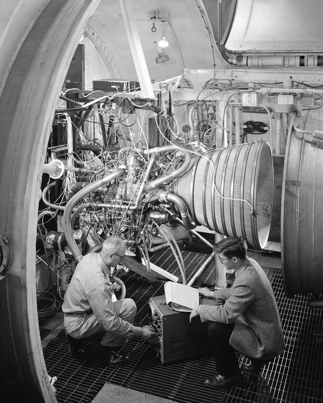 Two engineers kneeling down to examine medium sized rocket engine
