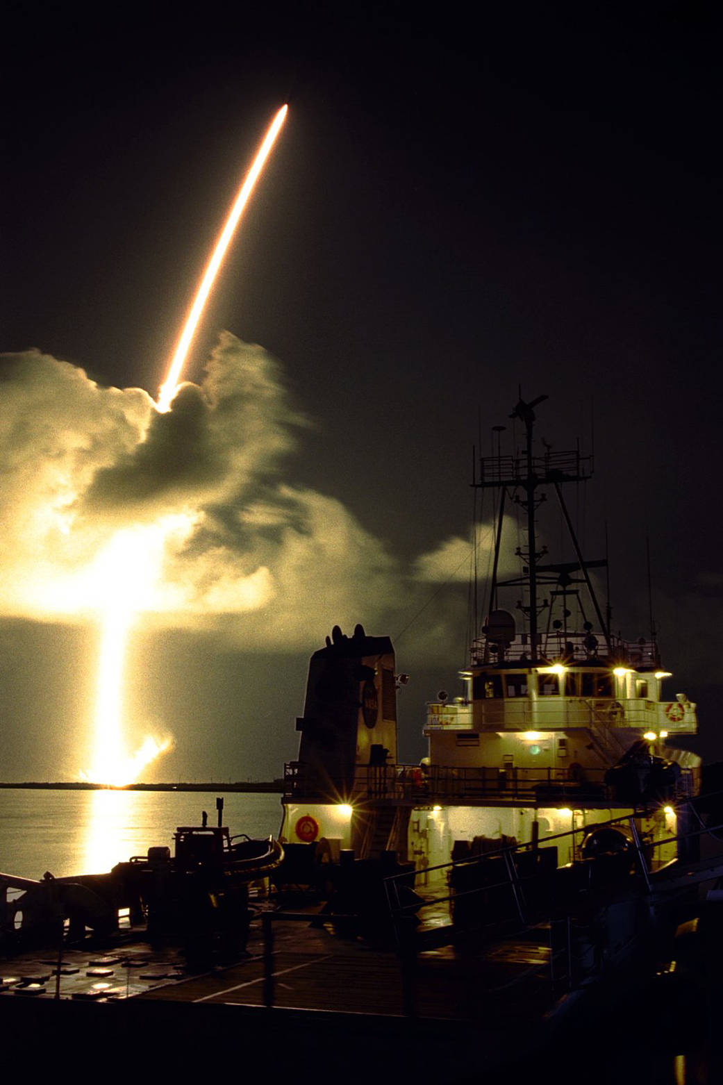 Nighttime launch of rocket with Cassini orbiter aboard seen from water with ship in foreground