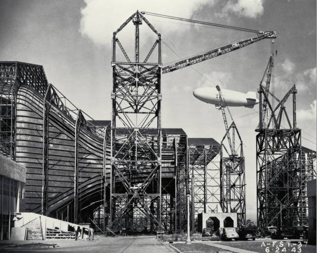 Construction of the Ames Full-Scale 40x80ft Wind tunnel. - side view of entrance cone, blimp in background.