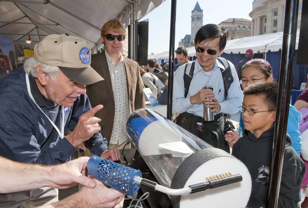 A NASA worker explaining wind tunnels to a young boy while his family looks on.