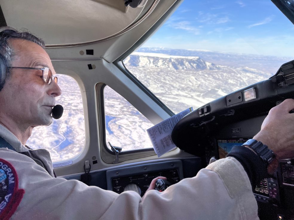 A pilot in the cockpit of an airplane during flight. Desert landscape and blue skies can be seen out the airplane windows.