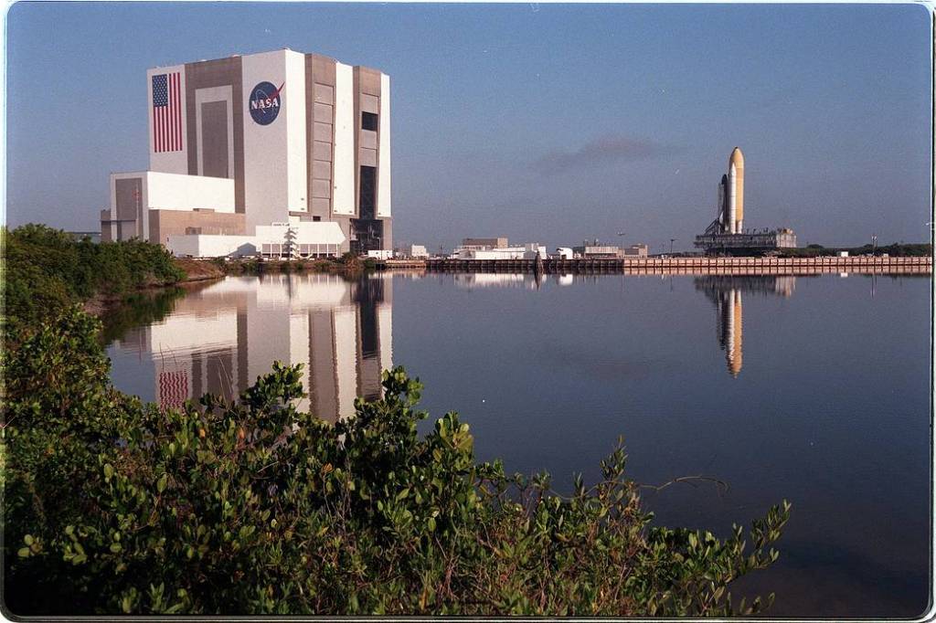 Reflected in the turn basin at the Launch Complex 39 area, shuttle Discovery and its mobile launcher platform stand atop the crawler-transporter.