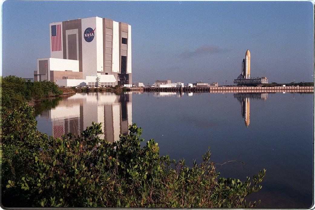 Reflected in the turn basin at the Launch Complex 39 area, shuttle Discovery and its mobile launcher platform stand atop the crawler-transporter.