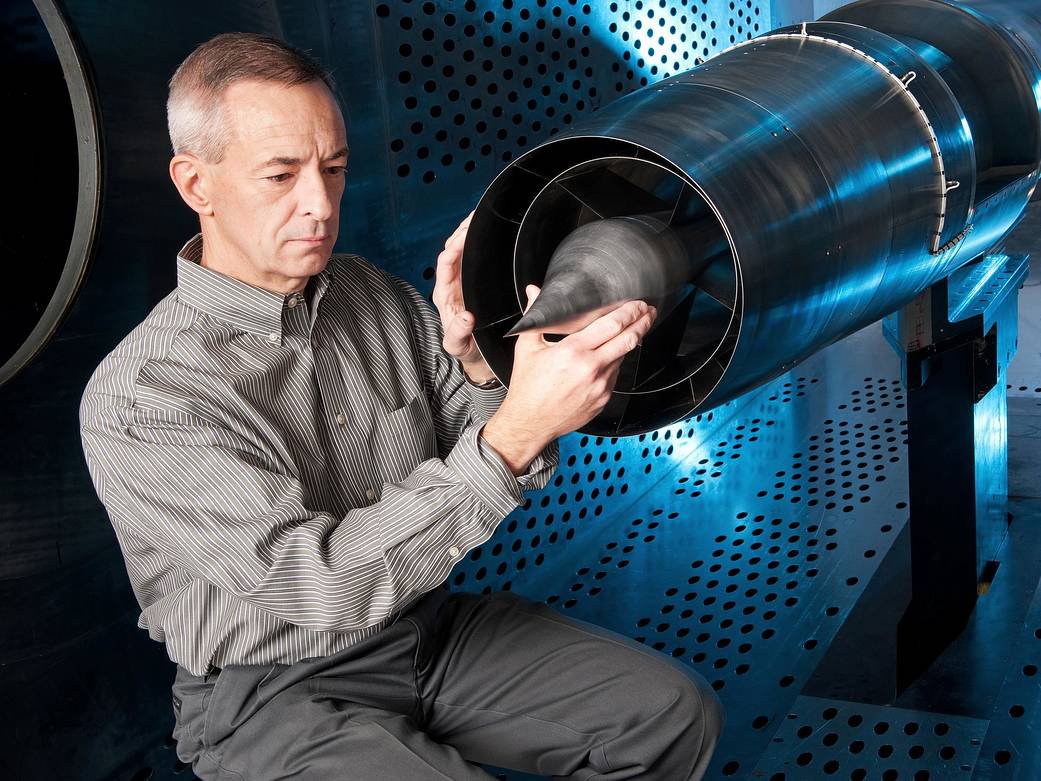 Technician in blue wind tunnel examining medium silver cylindrical model with pointed end