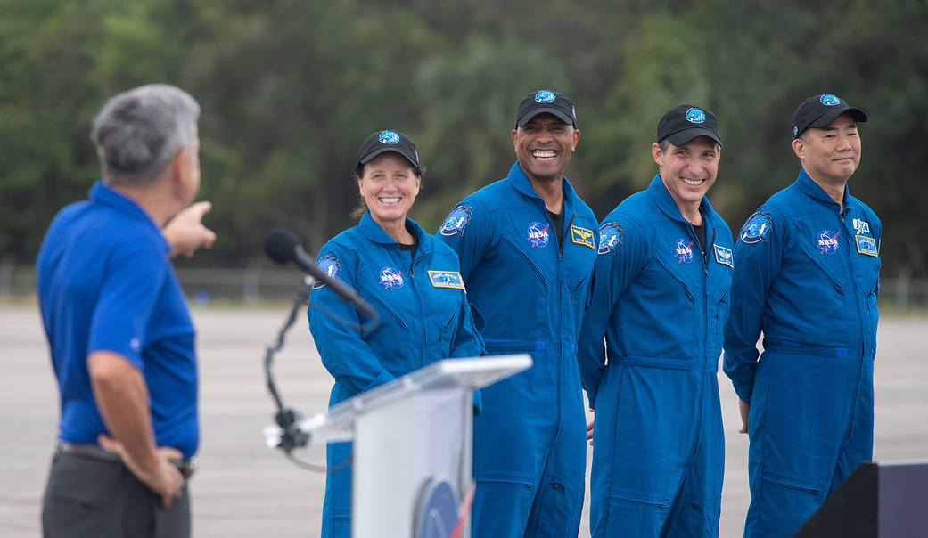 Four Crew-1 astronauts stand near podium