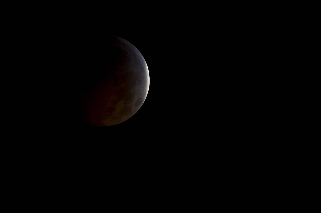 Moon during full eclipse with only a thin crescent illuminated against dark sky