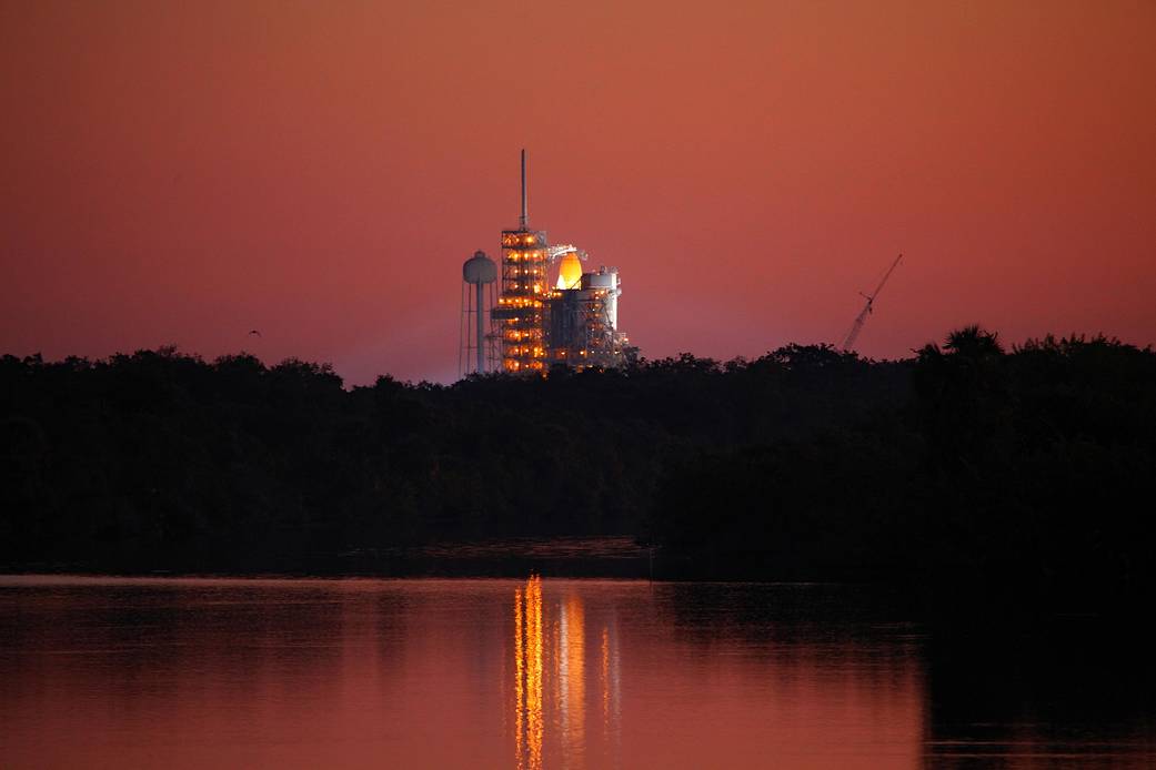 Shuttle Discovery vertical on launch pad with reflection visible in water