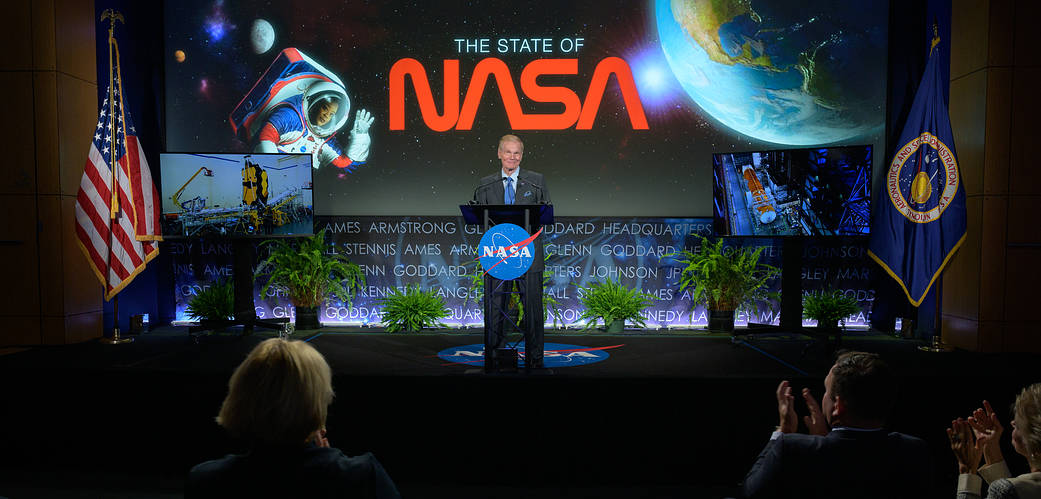 Bill Nelson standing at the podium delivering an address with the NASA Worm displayed behind him.