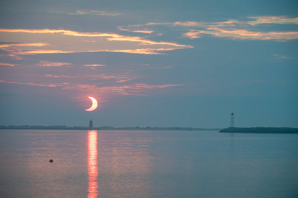 A partial solar eclipse is seen as the sun rises behind the Delaware Breakwater Lighthouse, Thursday, June 10, 2021, at Lewes Beach in Delaware. 