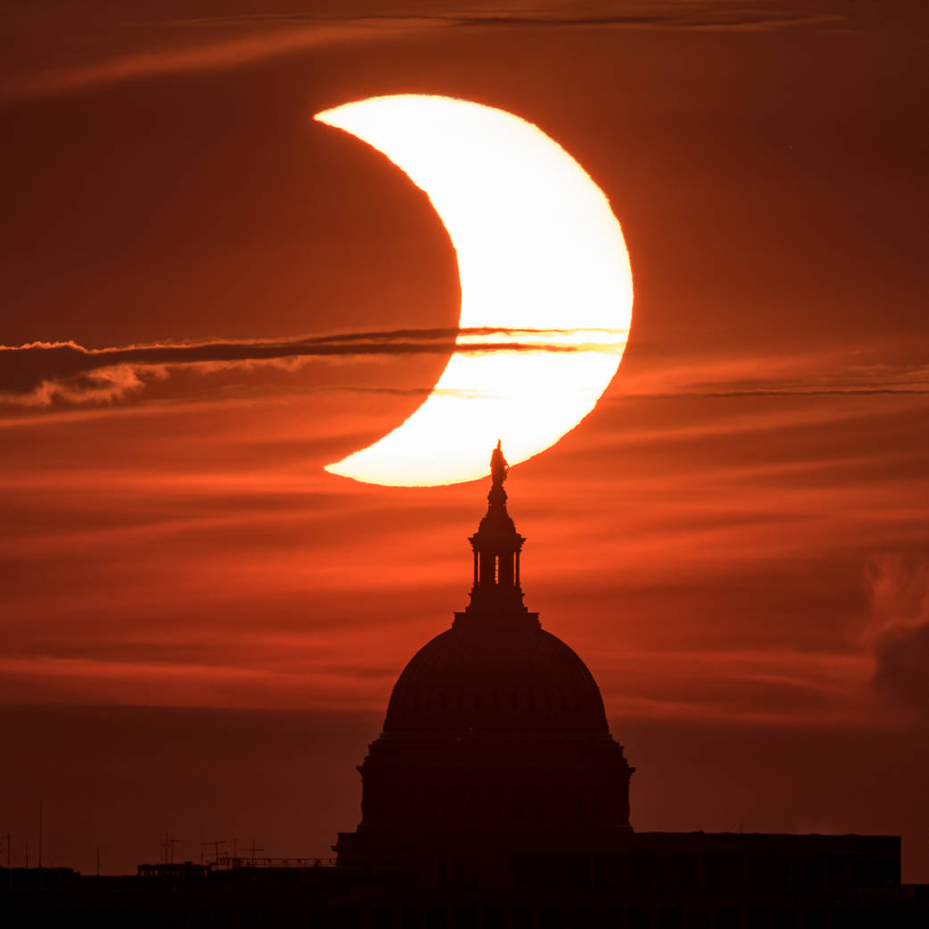 A partial solar eclipse is seen as the sun rises behind the United States Capitol Building, Thursday, June 10, 2021, as seen from Arlington, Virginia.