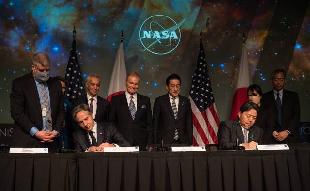 U.S. Secretary of State Antony Blinke and Japan’s Minister for Foreign Affairs, Hayashi Yoshimasa, seated at table sign agreement as officials from both nations stand. In the background are U.S. and Japan flags and NASA insignia.