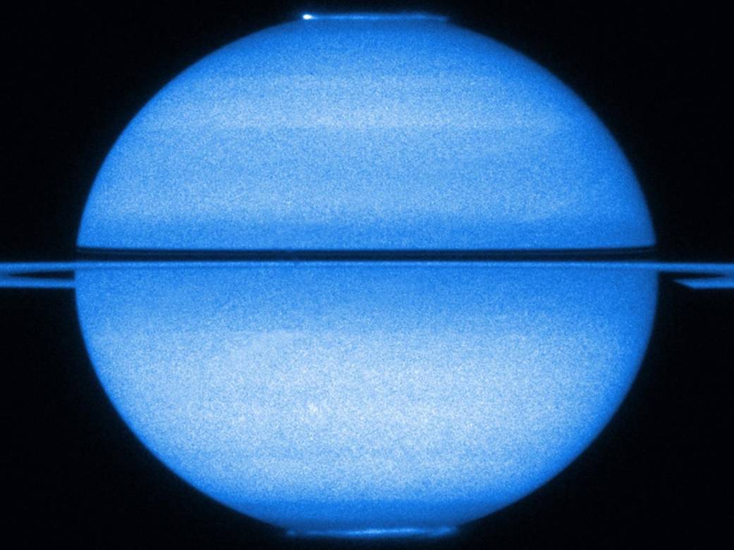 The planet Saturn in blue false color fills the frame with rings across at center