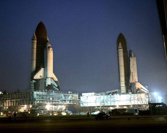 Space shuttle Atlantis, seen on the right, is parked in front of the Vehicle Assembly Building following its rollback from Pad 39A. On the left is space shuttle Columbia as it rolls by Atlantis on its way to the launch pad.