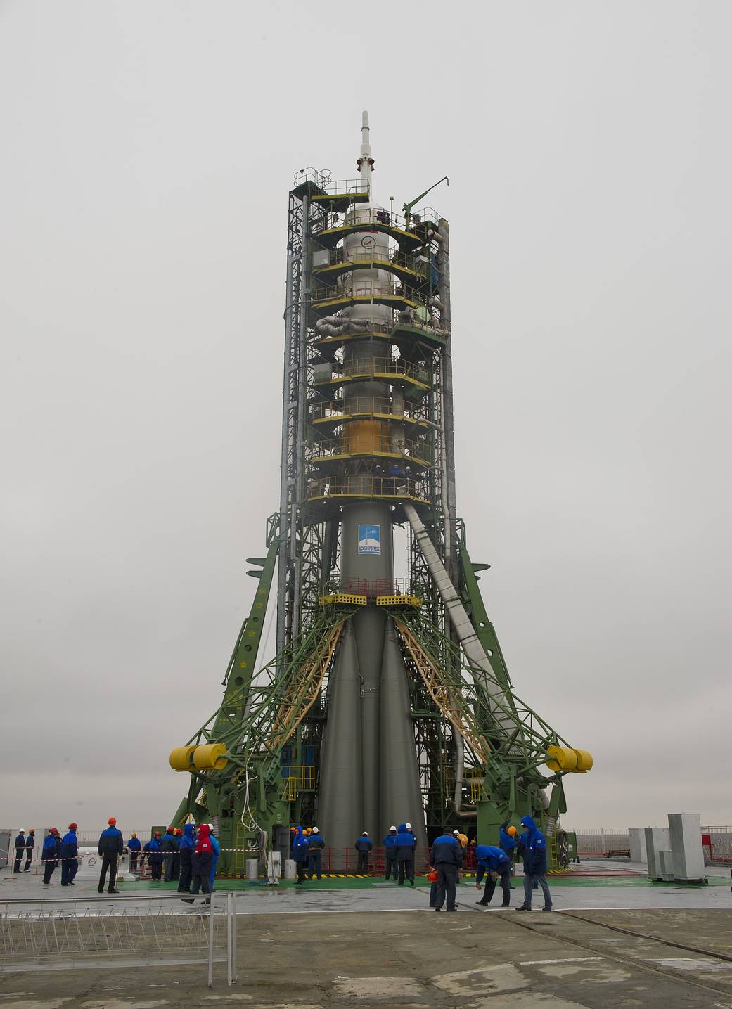 Soyuz rocket vertical at launch pad with tower surrounding, on cloudy day