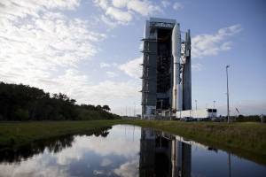 At Space Launch Complex 41, a pond reflects the 197-foot-tall United Launch Alliance Atlas V rocket and Vertical Integration Facility against a blue sky flecked with white clouds.