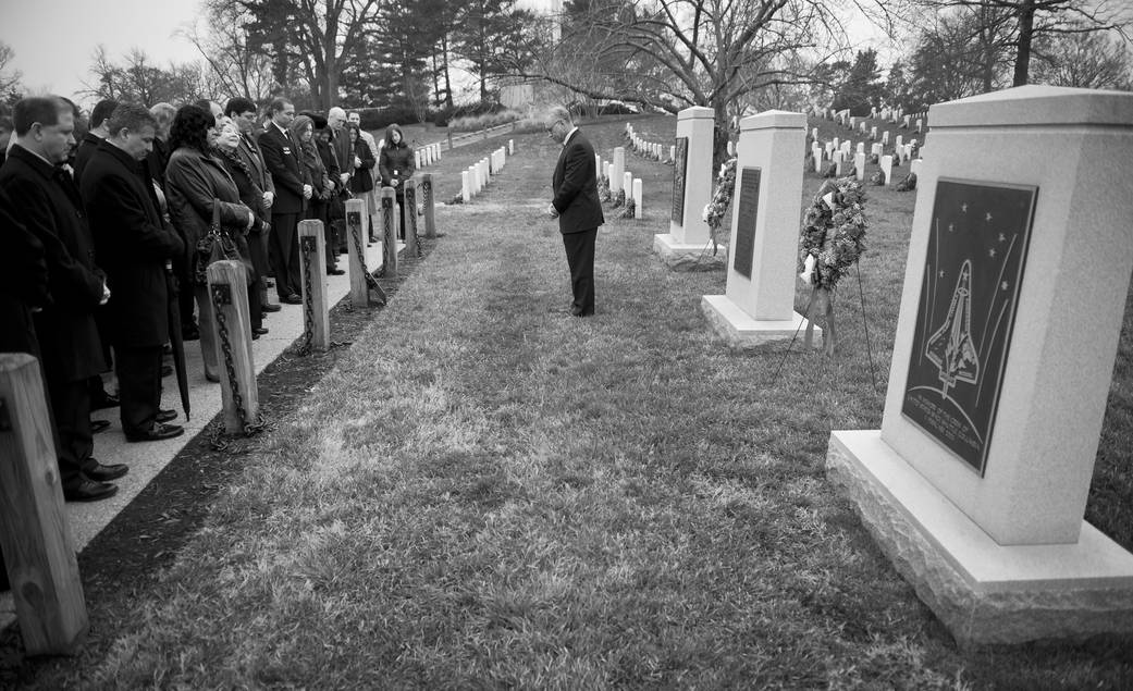 Black and white photo of cemetery with visitors standing in line at left for ceremony and man standing in center