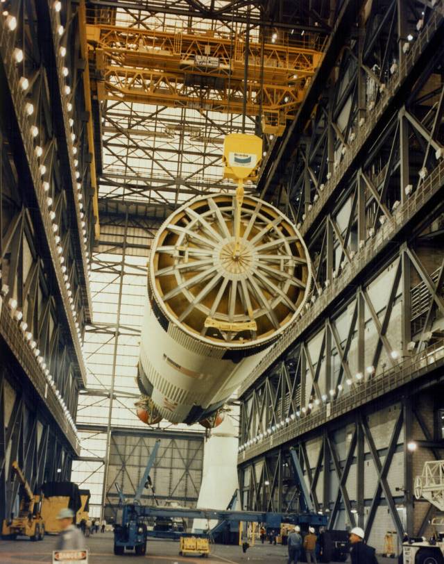 An overhead crane lifts the Saturn V first stage for the Apollo 11 mission from the transfer aisle floor in preparation for stacking on a mobile launcher inside the Vehicle Assembly Building's High Bay 1. 
