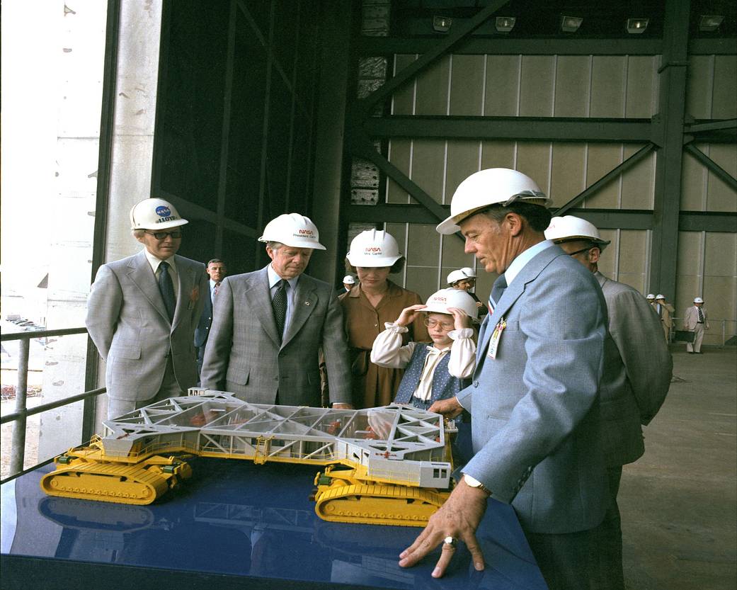 President Jimmy Carter, with wife Rosalynn and daughter Amy, listen to Lee R. Scherer, center director from 1974 to 1979, explain a model of the crawler-transporter during their tour of Kennedy Space Center.