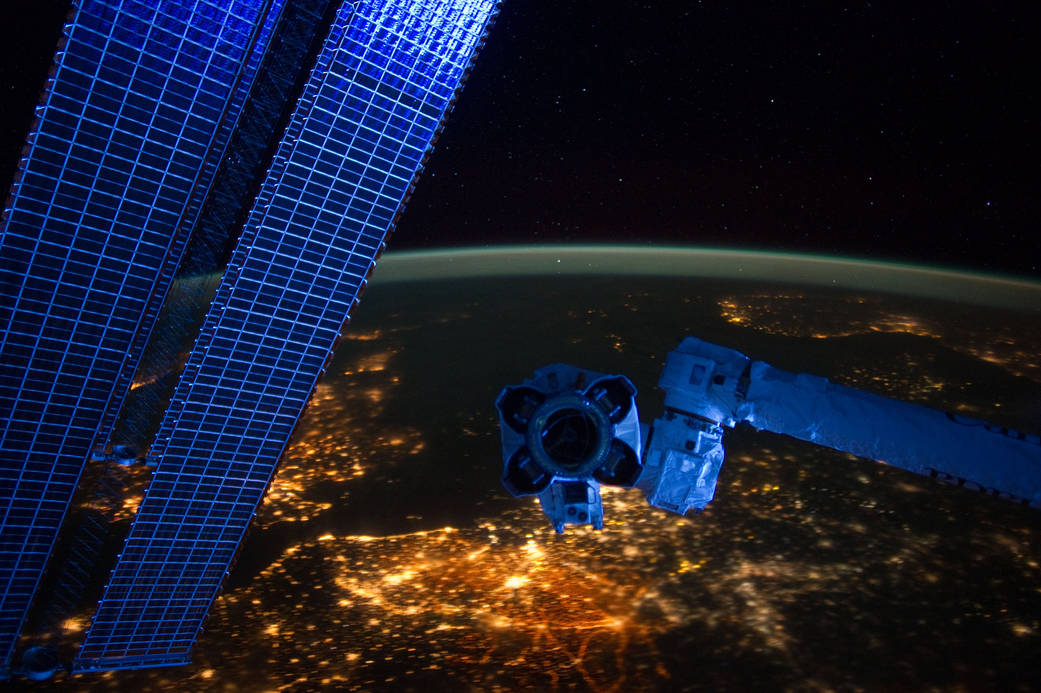 Brightly lit Western Europe photographed from Earth orbit with edge of atmosphere visible and space station solar arrays at left