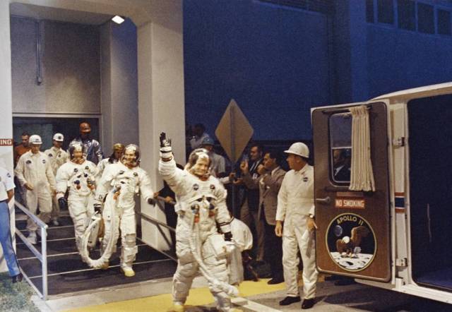 Apollo 11 Commander Neil A. Armstrong leads astronauts Michael Collins and Edwin E. Aldrin, Jr., from the Manned Spacecraft Operations Building to the transfer van for the eight-mile trip to Pad 39A.